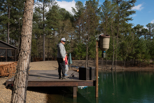 father and son fishing from a wooden dock beside a forested pond