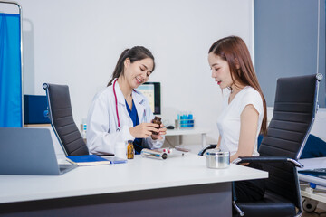 An Asian woman sits at a table consulting with a female doctor. They discuss her symptoms related...