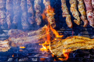 A grill filled with skewers and pork belly of meat cooking over open flames.