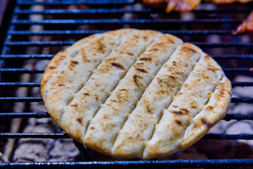 A piece of flatbread is being grilled, showing crisp grill marks. Its golden-brown surface highlights texture, capturing a delicious cooking moment.