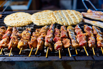A grill filled with skewers of meat cooking over open flames, fluffy pita bread grilling