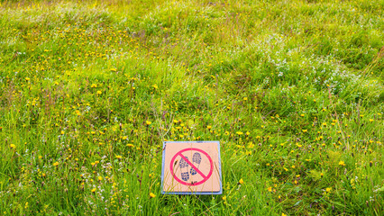 Signpost depicting footsteps crossed with red line in circle. Sign forbids hiking pathway, walking in nature. Nature is protected from entering.