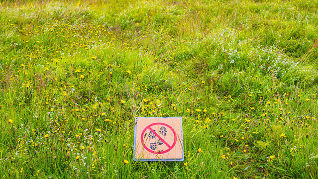 Signpost depicting footsteps crossed with red line in circle. Sign forbids hiking pathway, walking in nature. Nature is protected from entering.
