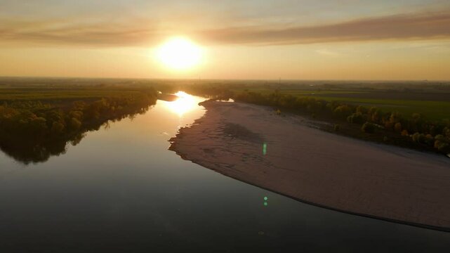 Slow-motion drone shot over dense forest lining riverbank at Isola Serafini where the Adda torrent merges into the Po beneath cirrostratus fibratus cloud sheets at sunset in Cremona
