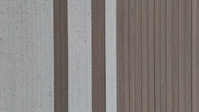 Alternating leveled and unleveled brown and grey soil bands stretch across the field under a slow-motion overhead drone revealing the precise texture and patterns of farmland prepared for seeding