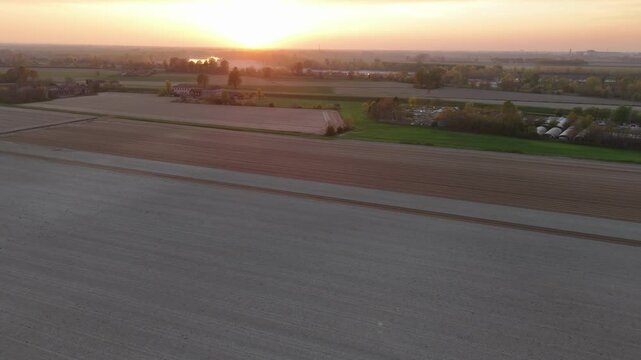 Sunset light casts warm hues across vast pre-seeded fields near Olza di Castelvetro Piacentino Italy, the drone pans revealing furrowed earth and distant barns in slow motion