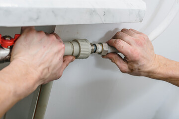 Closeup photo of man attaching pipe of heating system to radiator. Worker tightening pipe connections on a newly installed heating battery with a wrench