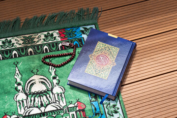 Holy Quran with Arabic calligraphy and wooden beads or tasbih with natural daylight and prayer mat...