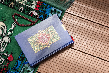 Holy Quran with Arabic calligraphy and wooden beads or tasbih with natural daylight and prayer mat...
