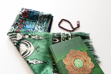 Holy Quran with Arabic calligraphy with wooden beads or tasbih and prayer mat below it on white...