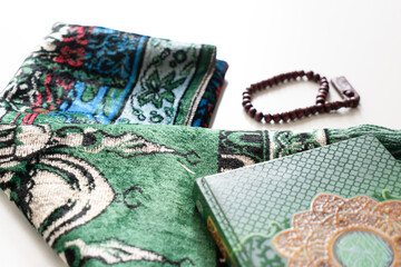Holy Quran with Arabic calligraphy with wooden beads or tasbih and prayer mat below it on white...