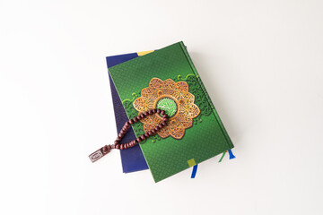 Pile of two Holy Quran with Arabic calligraphy with wooden beads or tasbih on white background