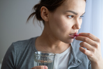 Asian pregnant woman is taking pills and vitamins for pregnant women with capsule on her hand and water. Drinking a tablet with a glass of water.