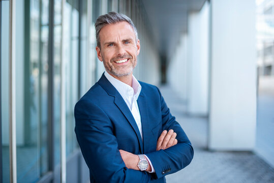 Smiling businessman in a suit standing outdoors with arms crossed