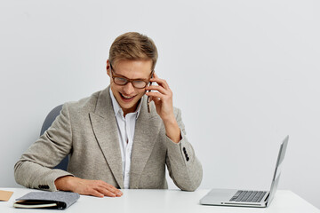 Smiling man wearing glasses in a gray blazer working at his desk with a laptop and documents,...