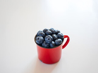 Fresh, raw blueberries in a  red metal or tin cup, on a white background. Top down view,no people