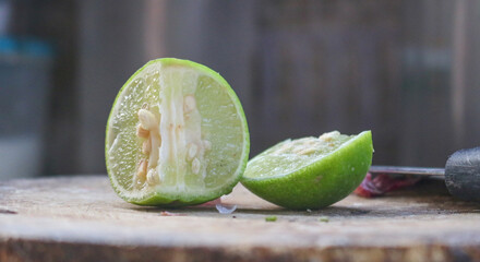 Lime halved on a wooden cutting board with a knife next to it. Food ingredient concept, sour...
