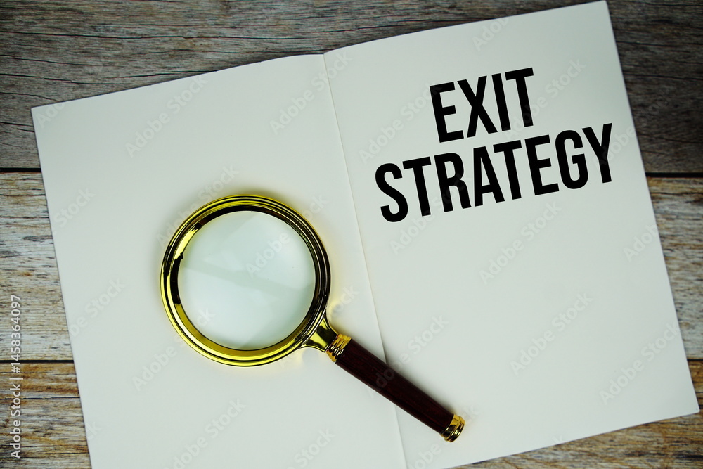 Poster exit strategy text message written on paper note with magnifying glass top view on wooden background