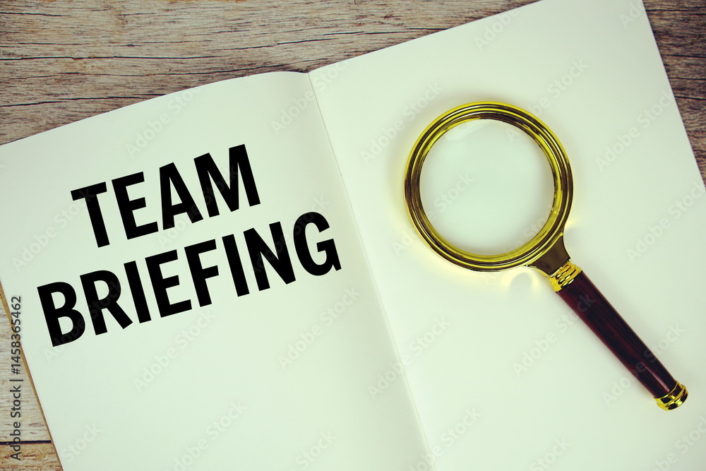 Poster team briefing text message written on paper note with magnifying glass top view on wooden background