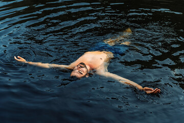 Relaxed man floating in natural dark water outdoors
