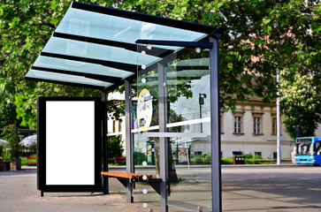 bus shelter at a busstop. blank billboard ad display. empty white lightbox sign. glass and aluminum frame structure. city transit station. bench inside. urban street setting. outdoor advertising