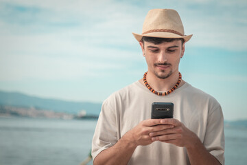 Handsome man holding mobile phone in his hand and texting message, on tropical background