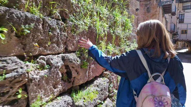 Tourist woman touching the plants that come out of the stone walls in the medieval village of Beceite, Teruel.