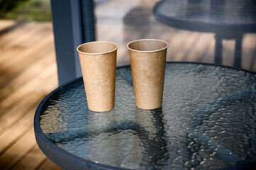 Disposable paper coffee cup with black lid placed on a glass table outdoors. Conceptual image for...