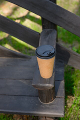Fototapeta premium Disposable paper coffee cup with black lid, outdoors. Conceptual image on the topic of takeaway lifestyle, modern urban habits, eco-friendly packaging and morning coffee rituals.