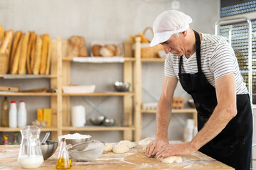 Experienced male baker kneads dough and shapes baguettes for baking in oven