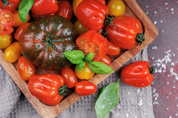 Colorful heirloom tomatoes with fresh basil on a rustic tray, water droplets and salt highlighting natural and healthy food concepts