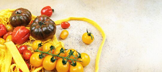 Yellow and red tomatoes with heirloom varieties in yellow mesh grocery bag on rustic stone surface