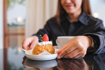 Closeup image of a woman serving a plate of strawberry choux cream in cafe