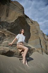 woman stands confidently on a large rock at a coastal area, basking in sunlight