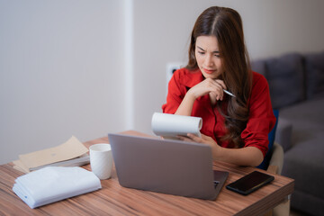 Young asian businesswoman working from home is checking receipts and calculating expenses using...