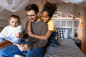 Excited single father plays with diverse, multi-ethnic daughters. Using digital tablet enjoy weekend