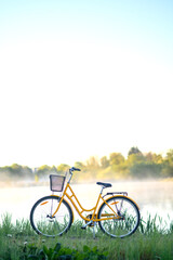Beautiful yellow bicycle near a pond or a lake with fog, steam, wist over water.