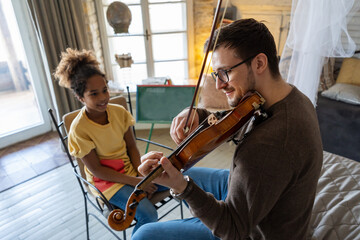 Young man musician teaching a teen girl to play violin. Education music instrument happiness concept