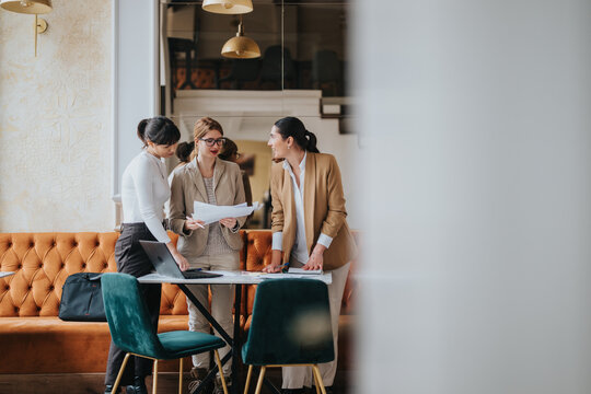 Three women in business attire discussing documents in a stylish and modern office.