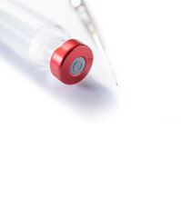 Thin syringe lies next to a vaccination or injection bottle with red cap on a white background. Space for text and design