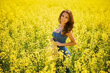 Fototapeta premium beautiful woman with a hat posing in the blooming rapeseed field on a sunny day