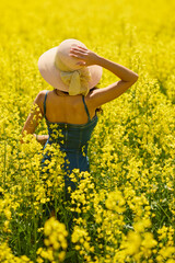 Fototapeta premium beautiful woman with a hat posing in the blooming rapeseed field on a sunny day