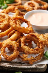 Deep fried onion rings on wooden board with sauce