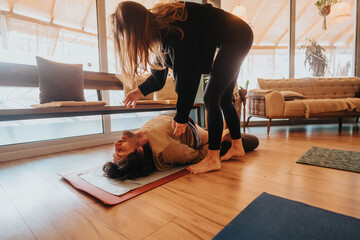 A relaxing yoga practice where an instructor guides a student through a stretch, set in a cozy, naturally lit studio.