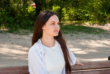Young caucasian female in a white shirt with long brown hair sits pensively on a park bench...