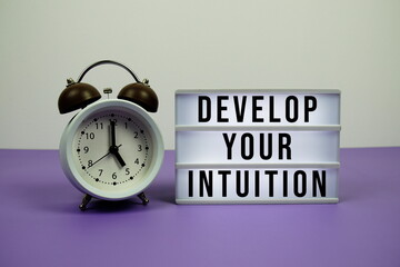 Develop Your Intuition text on LED lightbox with alarm clock on purple background