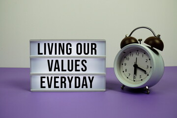 Living our values everyday text on LED lightbox with alarm clock on purple background