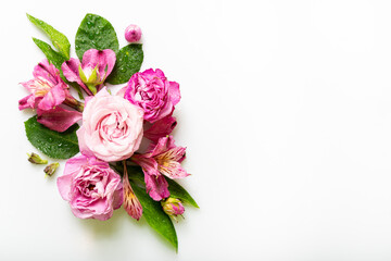 Fresh bouquet with pink and purple flowers, highlighted by water droplets, surrounded by green leaves on a white background