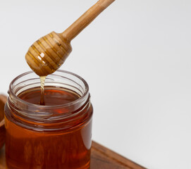 Close up shot of honey dripping from honey dipper in a jar of honey