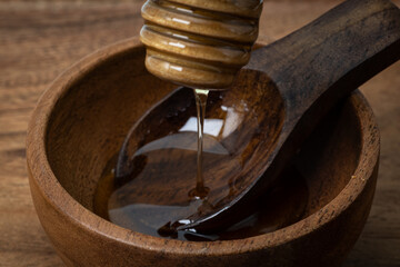 Close up of honey dripping from a dipper in a wooden bowl with a wooden spoon